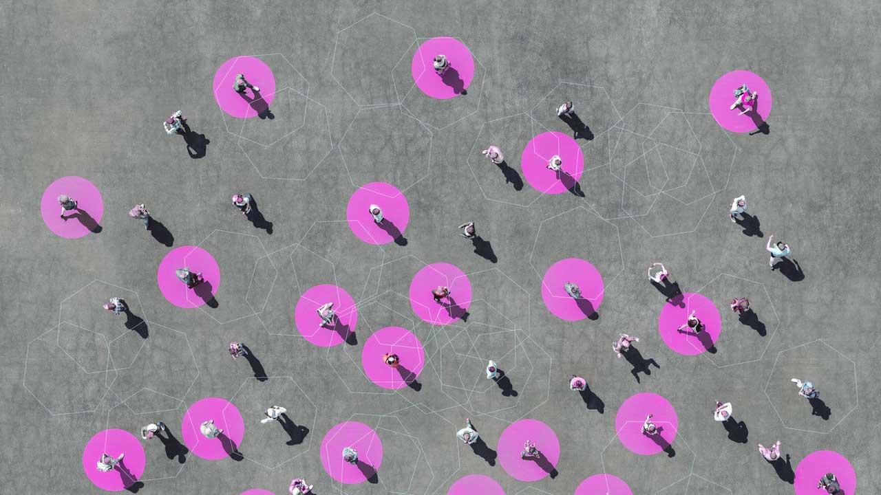 Aerial view of people standing on a gray surface, several are highligted within bright pink circles. Long shadows suggest sunlight.