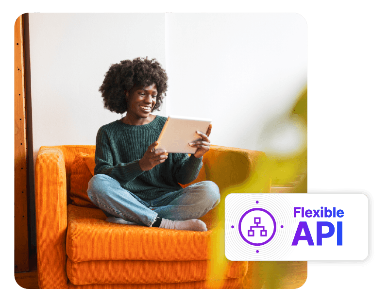 A "Flexible API" dashboard badge with an organizational chart icon, overlaid on a background photo of a smiling Black woman sitting cross-legged on a bright orange armchair while looking at a tablet.