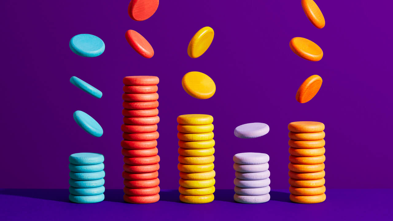 Stacks of colorful wooden tokens with coins falling from above on a purple surface, illustrating strategies to optimize market research budgets.