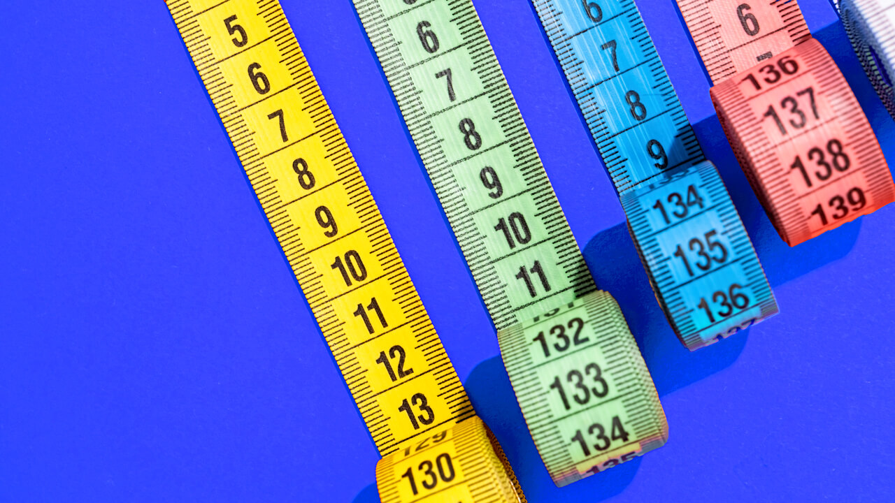 An overhead flat-lay illustration featuring four colorful coiled measuring tapes in yellow, light green, blue, and coral pink lined up on a vibrant royal blue surface, representing Cint's article evaluating the best ad effectiveness and media measurement tools in 2026.